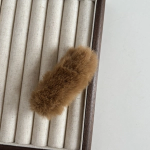 Vue détaillée d'une pince à cheveux en peluche marron sur un support minimaliste