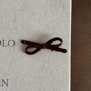 Gros plan d'une pince à cheveux nœud rouge foncé brillant en résine sur une carte beige