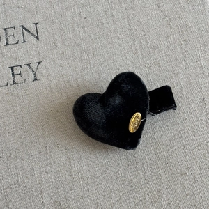 Close-up of a heart-shaped black velvet hair clip featuring an elegant golden Love metal tag