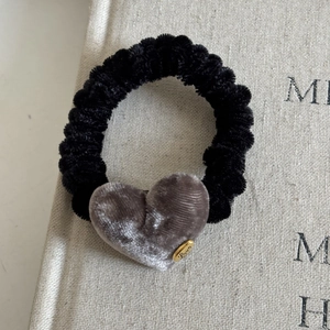 Close-up of velvet heart charm and golden 'Love' tag on black textured scrunchie