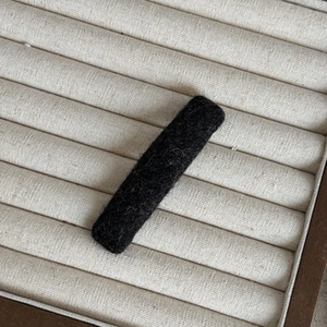 Close-up of black fuzzy fabric hair clip featuring soft plush texture on beige tray