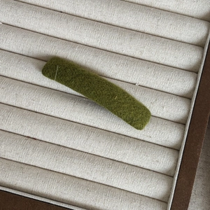 Close-up of moss green herringbone fabric hair clip on a beige linen display tray