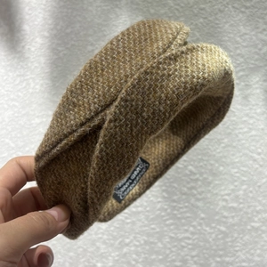 Détail de la texture en tweed marron du serre-tête avec étiquette interne en main