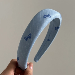 Light blue striped headband with bow pattern held in hand against a grey background