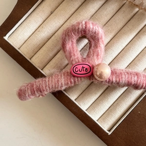 Gros plan sur une pince à cheveux en peluche rose avec étiquette et perle douce