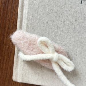 Détail d'une barrette en feutre rose avec nœud crème sur un livre neutre