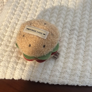 Detail view of a plush sponge cake hair clip with fabric label on a white crochet rug