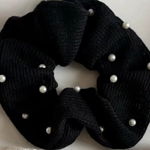 Detail of a black scrunchie made of fine knit fabric decorated with white pearls
