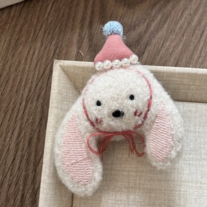 Close-up of a plush white puppy hair clip with a pink knitted hat and pearl accents