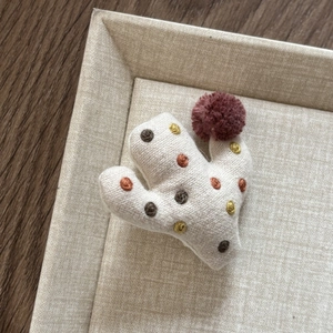 Detail of handmade fabric cactus hair clip with embroidery and a red pompom accent