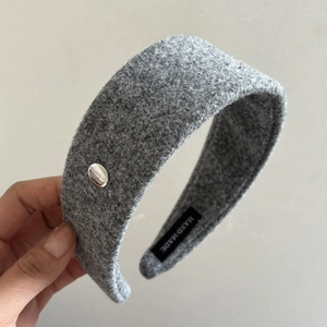 Detail of grey woolen headband featuring engraved metal charm and handmade textile label