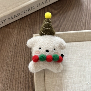 Detailed close-up of a plush puppy hair clip with a green knit hat and festive pom-poms