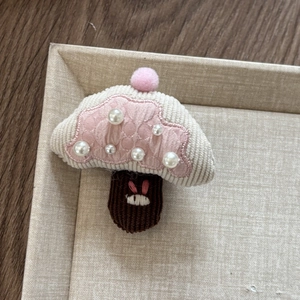 Detailed macro view of a corduroy mushroom hair clip with pearls and a pink pompom