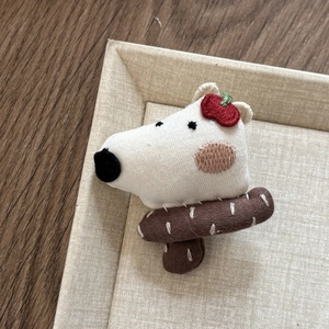 Close-up of handmade plush puppy brooch with red apple embroidery and knitted scarf
