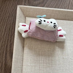 Close-up of pink and white plush Hello Kitty candy hair accessory on a beige tray