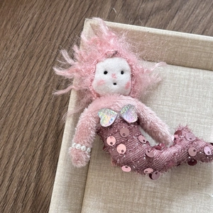 Detail of handmade crochet mermaid doll with pink sequins and pearl bracelet