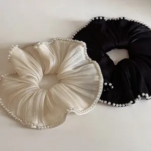Detailansicht von cremefarbenen und schwarzen Satin-Haargummis mit Perlensaum