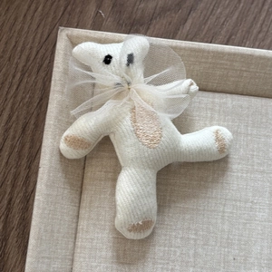 Close-up of cute white plush bear hair clip with mesh bow on a textured display tray