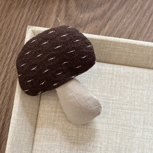 Detailed close-up of a handmade brown mushroom hair clip with white embroidery details