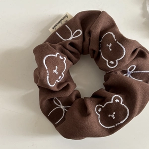 Detail view of brown fabric scrunchie with cute bear embroidery and handmade label