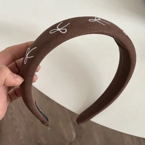 Detail view of a brown wide headband with white embroidered bows and black non-slip lining