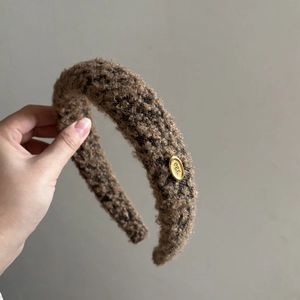 Brown faux shearling headband with golden 'egg' label for a high-volume hair look
