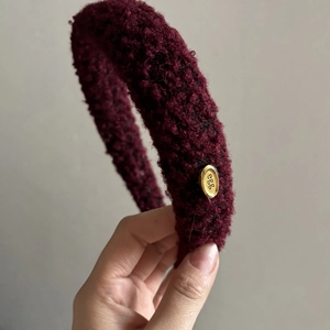 Close-up of a burgundy plush sponge headband with golden egg logo metal detail