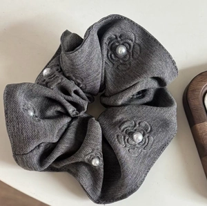 Detailed view of dark grey textured fabric hair tie with floral embroidery and pearls