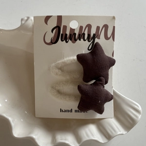 Close-up of handmade brown star fabric hair clips with white plush on display card