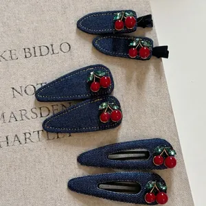 Set de barrettes en denim bleu foncé avec cerises rouges et strass sur fond de livre vintage