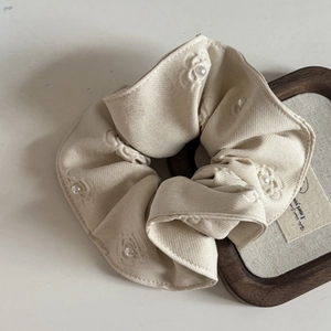 Close-up of beige fabric scrunchie featuring embroidered flowers and faux pearls decoration