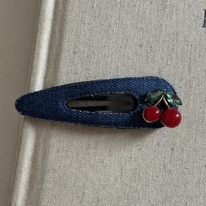 Barrette en denim bleu foncé avec des strass cerises rouges sur un fond beige doux