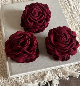 Detailed view of three deep red fabric rose hair clips on a minimalist book background