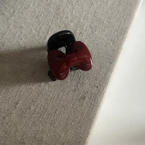 Détail d'une pince à cheveux à nœud rouge avec base noire sur fond de tissu clair