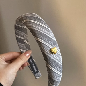 Detail of grey striped padded headband featuring a gold heart charm and handmade label