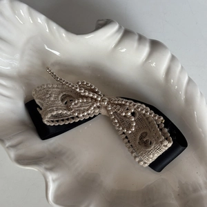 Vintage lace and pearl bow hair clip with black silk ribbon on a white ceramic shell tray