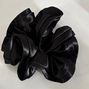 Detail of elegant black satin scrunchie with voluminous ruffles and silk texture