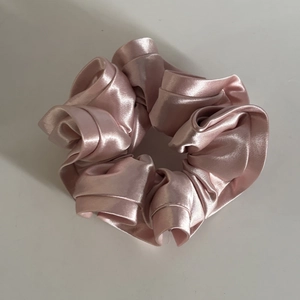 Detailed close-up of pink satin scrunchie with layered ruffle design and silky texture