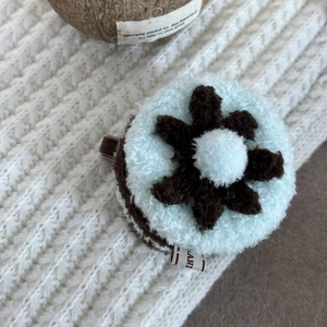 Close-up of a blue plush flower hair clip with a stylish fabric label on cozy knitwear