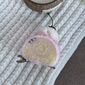 Detailed view of pink cherry Swiss roll plush hair clip with a handmade label on knit fabric
