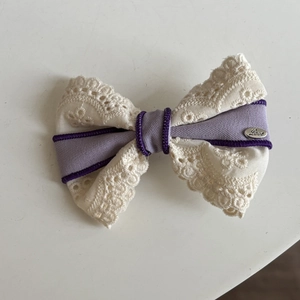 Détail d'une pince à cheveux avec nœud en dentelle violette et charme en métal gravé Love