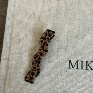 Detail of leopard print wavy acetate duckbill hair clip on textured beige fabric