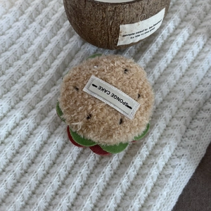 Detailed view of the plush hamburger hair clip with sponge cake tag on white knit fabric