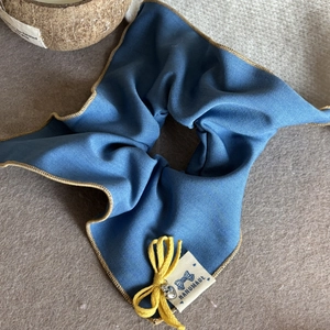 Détail d'un chouchou en tricot bleu avec nœud jaune, clochette et étiquette fait main