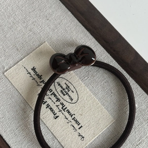Macro shot of a dark brown bow hair tie on rustic linen fabric with wooden frame detail
