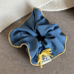 Détail d'un chouchou bleu avec nœud jaune, breloque cœur et étiquette fait main en tissu