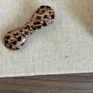 Detailed top view of a glossy leopard print hair clip on textured beige fabric material