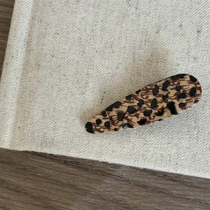 Detailed view of teardrop leopard print hair clip on a minimalist textured surface