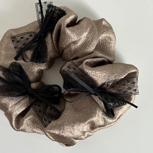 Elegant bronze metallic satin scrunchie with black lace bow accents on white background