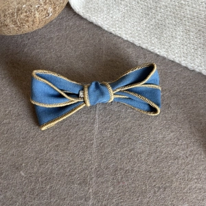 Détail du nœud à cheveux en denim bleu avec coutures dorées et pince en métal argent